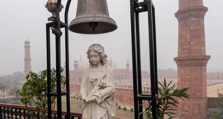 Statue de marbre sous une cloche surplombant les minarets d'une mosquée dans un complexe historique brumeux.