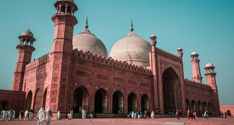 Majestueuse mosquée Badshahi avec de grands dômes et des murs complexes en grès rouge contre un ciel dégagé.