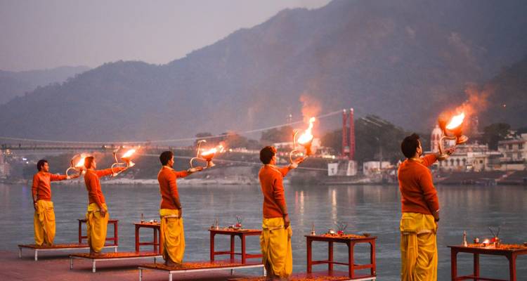 Prêtres effectuant l'Aarti du Gange du soir avec des lampes enflammées sur la rive contre des silhouettes de montagnes.