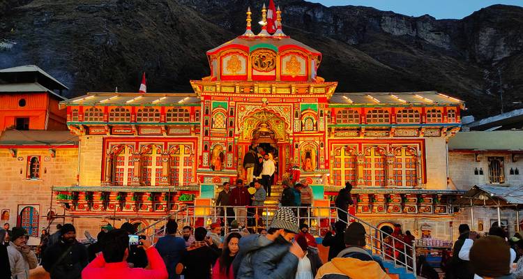 Façade aux couleurs vives du temple de Badrinath rayonnant dans la lumière du soir avec des dévots rassemblés à l'extérieur.