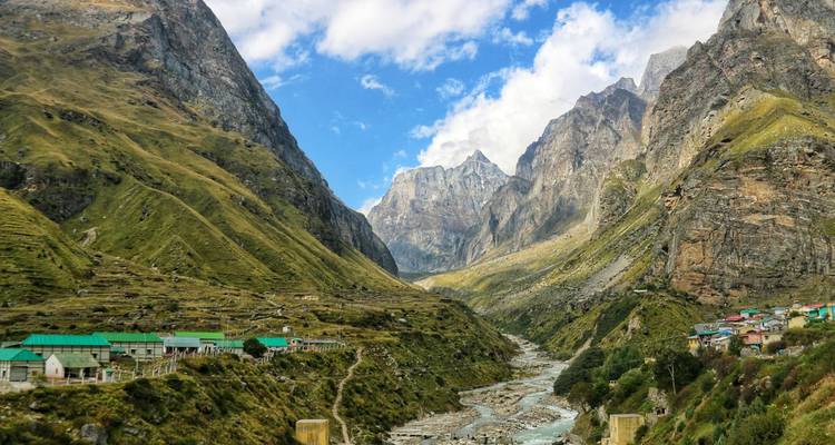 Vallée de montagne spectaculaire avec une rivière serpentant à travers des prairies alpines sous un ciel lumineux.