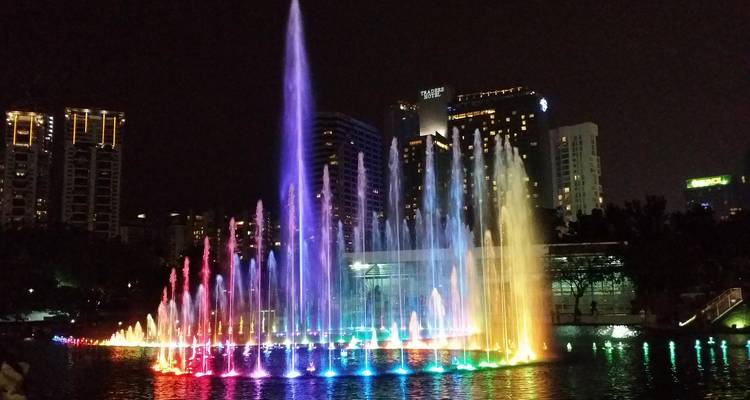 Spectacle nocturne de fontaines illuminées aux couleurs de l'arc-en-ciel devant l'horizon des gratte-ciel de Kuala Lumpur.