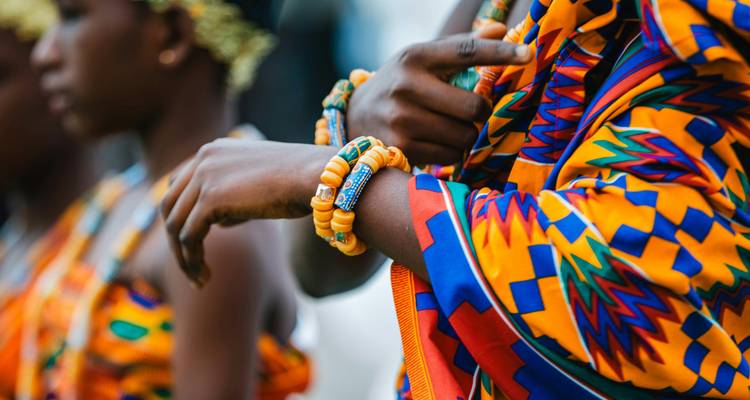 Gros plan de femmes portant des tissus Kente colorés et des bracelets de perles lors d'une cérémonie traditionnelle.