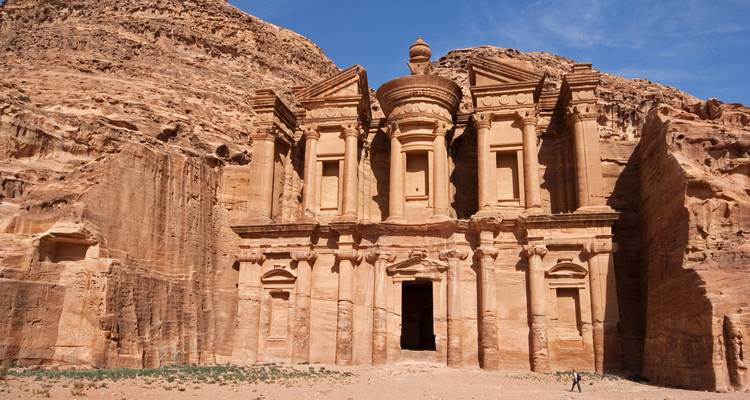 Traveler dwarfed by the majestic façade of the Monastery carved into rose sandstone cliffs at Petra
