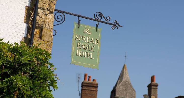 Enseigne suspendue traditionnelle de l'hôtel The Spread Eagle contre un ciel anglais bleu clair.