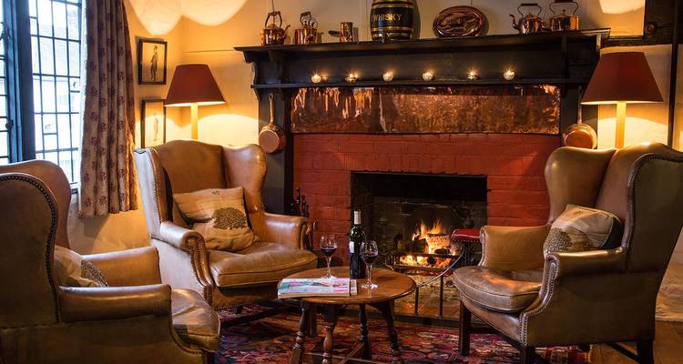 Salon douillet avec fauteuils, cheminée crépitante et éclairage chaleureux dans un hôtel de campagne anglais.