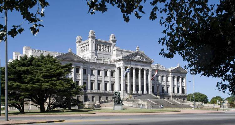 Neoclassical Palacio Legislativo with grand columns and Uruguayan flags on a sunny day in Montevideo.