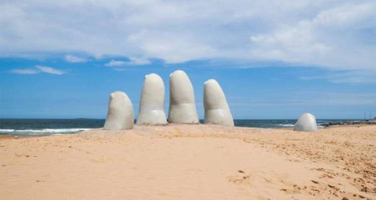 Famous Hand of Punta del Este sculpture emerging from golden beach sand against blue sky.