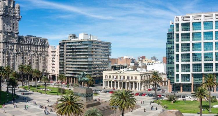 City square with mix of historic and modern buildings, palm trees and people walking around.