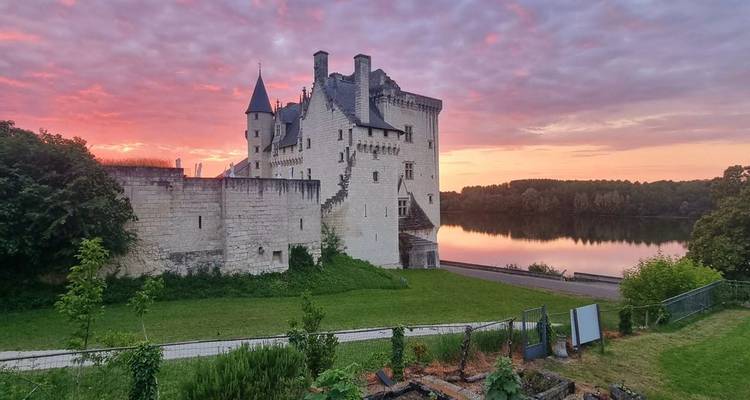 Märchenschloss am Flussufer, das bei Sonnenaufgang leuchtet, mit farbenfrohem Himmel, der sich im ruhigen Wasser im Loire-Tal spiegelt.