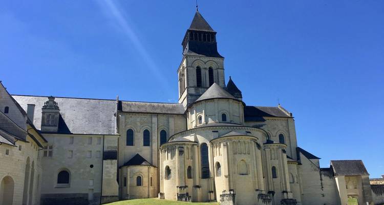 Romanische Abtei mit Schieferdächern und zentralem Turm unter klarem blauen Himmel in der Loire-Region.