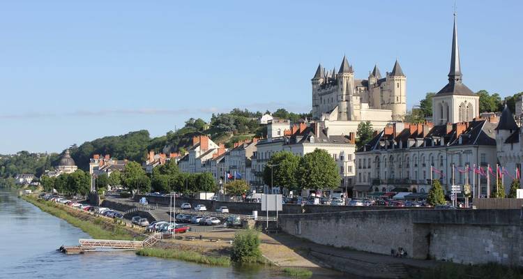 Panoramablick auf Saumur vom Fluss aus mit dem Schloss auf dem Hügel und einer Reihe historischer Häuser am Flussufer.