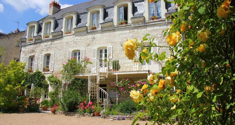 Charmantes Steinpensionat mit blühenden gelben Rosen und Garten an einem sonnigen Tag.