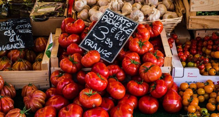 Tomates provenzales apilados en un puesto vibrante de mercado francés con letrero de pizarra escrito a mano.
