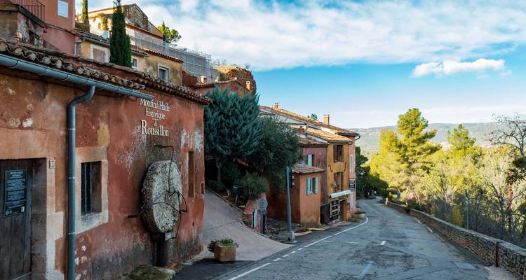 Calle silenciosa de color ocre en el pueblo de Roussillon con fachadas rústicas bajo un cielo azul.