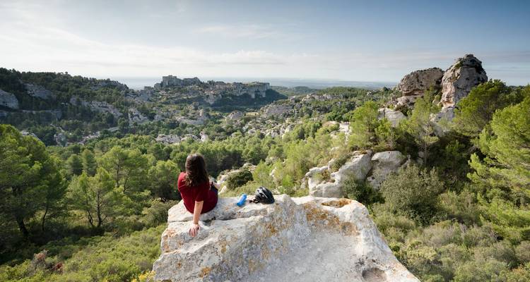 Excursionista sentado en un mirador rocoso contemplando el dramático paisaje de piedra caliza de Les Baux-de-Provence.