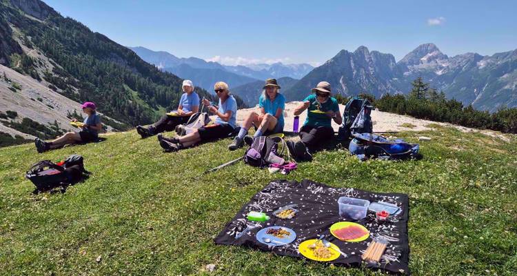 Les randonneurs profitent d'un pique-nique dans une prairie alpine entourée de pics slovènes déchiquetés sous un ciel dégagé.