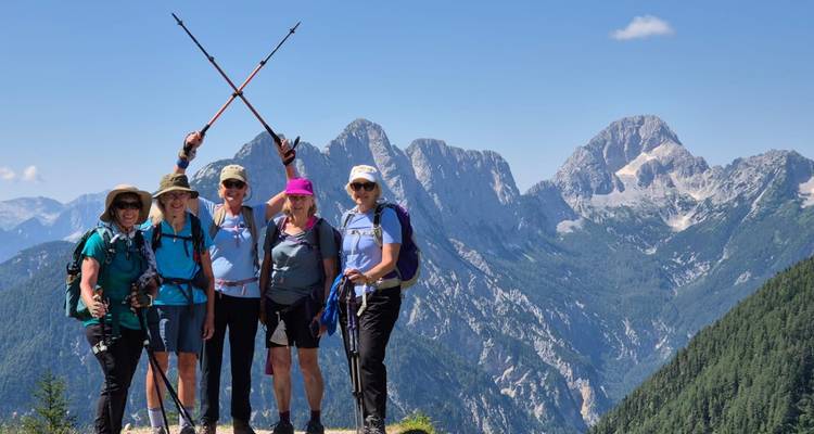 Cinq randonneurs posant avec des bâtons de randonnée croisés sur une crête de montagne avec des pics alpins spectaculaires en arrière-plan.