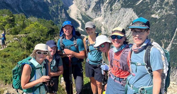 Groupe de randonneurs debout au bord d'une falaise avec des bâtons de randonnée, falaises escarpées et vallées en arrière-plan.