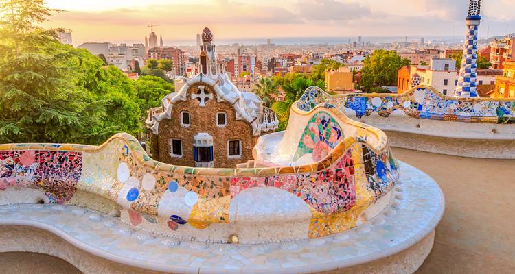 Colourful mosaic benches overlooking the city skyline from Park Güell at sunrise.