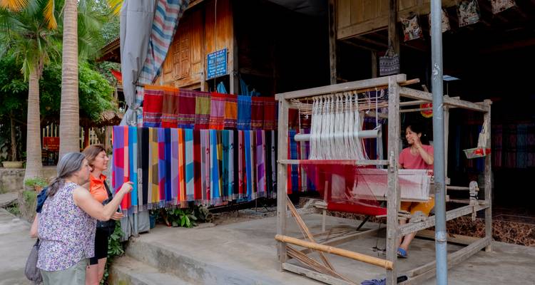 Les visiteurs regardent un artisan local tissant un tissu coloré sur un métier à tisser traditionnel.