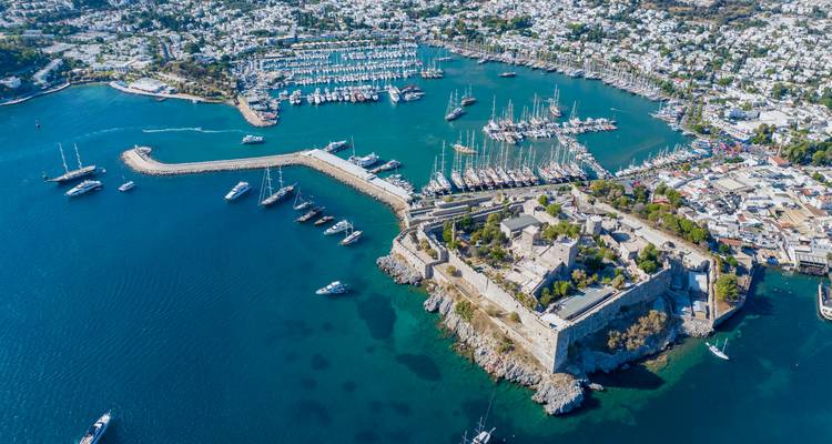 High aerial of Bodrum harbour with medieval castle, marinas and deep blue sea dotted with yachts.