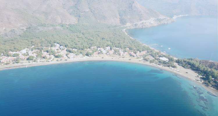 Hazy aerial of a wide shallow bay bordered by forested hills and a small seaside village.