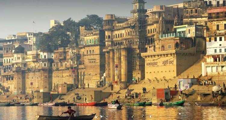 Botes coloridos y multitudes se reúnen en los históricos ghats del río con grandes edificios de arenisca que se alzan a lo largo del Ganges.