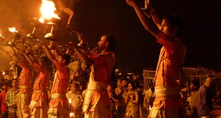 Sacerdotes en túnicas azafrán realizan una ceremonia nocturna de Ganga Aarti con antorchas encendidas ante una gran multitud.