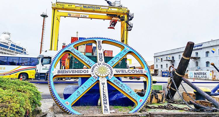Decoratief industrieel wiel bij de haven van Montevideo dat bezoekers verwelkomt in meerdere talen.