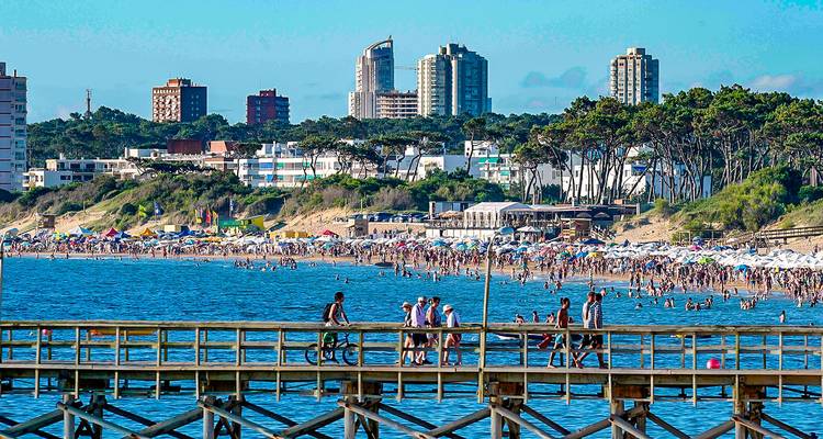 Druk zandstrand en lange pier met fietsers tegen de skyline van Punta del Este.