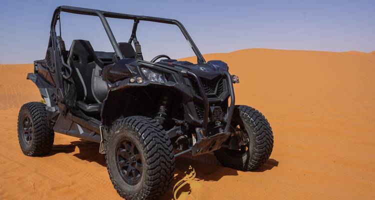 Un buggy des dunes noir garé sur des dunes de sable orange vif sous un ciel dégagé.