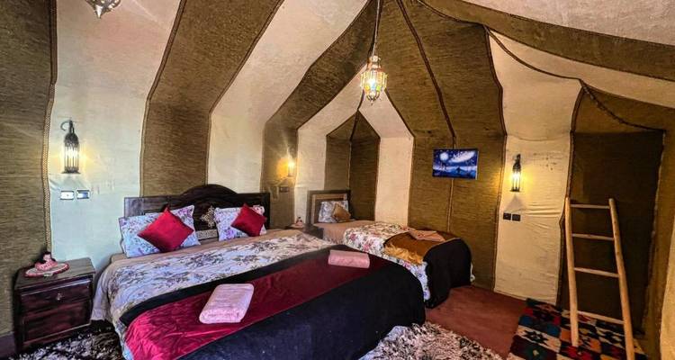 Hébergement en tente du désert confortable avec tapis colorés, lits jumeaux et doubles, et éclairage à la lanterne.