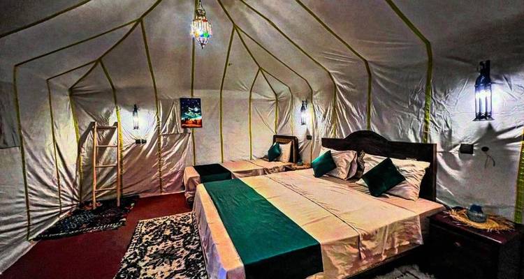 Tente de désert spacieuse en toile blanche avec deux grands lits et un éclairage d'ambiance doux.