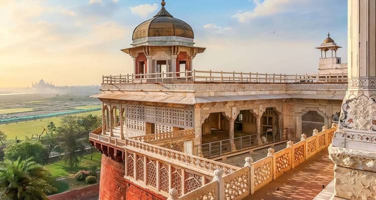 Elegante balcón de mármol y pabellón abovedado del Fuerte de Agra con vista al río Yamuna al atardecer.