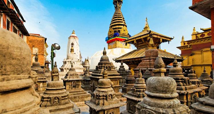 Stupa de Swayambhunath rodeada de santuarios de piedra y banderas de oración contra un cielo azul brillante.