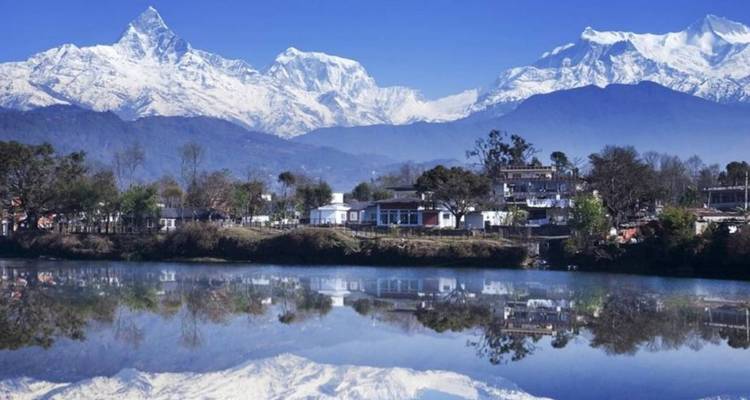 La cordillera de Annapurna cubierta de nieve se refleja perfectamente en un lago tranquilo cerca de Pokhara en un día despejado.