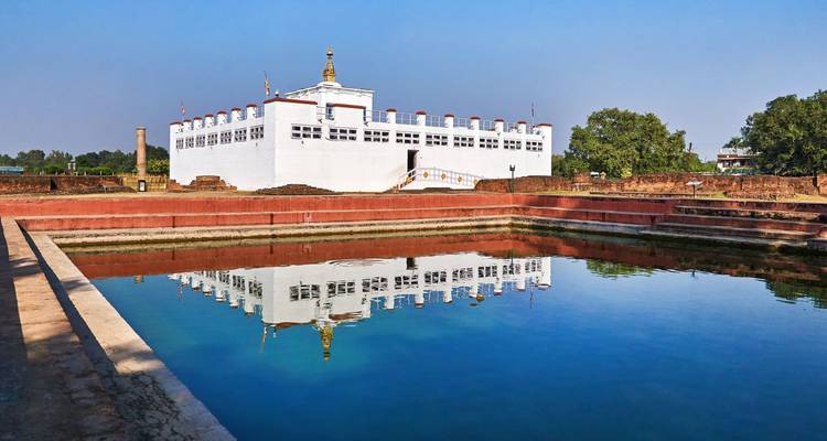 Templo blanco de Maya Devi en Lumbini reflejado en una piscina reflectante rectangular bajo un cielo azul despejado.
