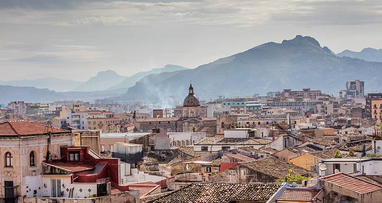 Vue panoramique de midi brumeuse sur les toits d'une ville sicilienne avec des montagnes escarpées distantes formant l'arrière-plan.