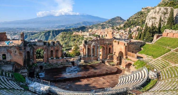 Vue panoramique du théâtre grec antique de Taormine surplombant la côte luxuriante avec l'Etna enneigé au-delà.