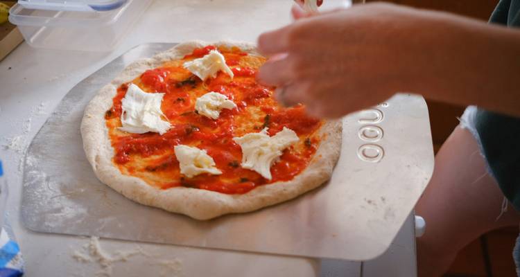 Primer plano de una base de pizza siendo cubierta with salsa de tomate y queso fresco.