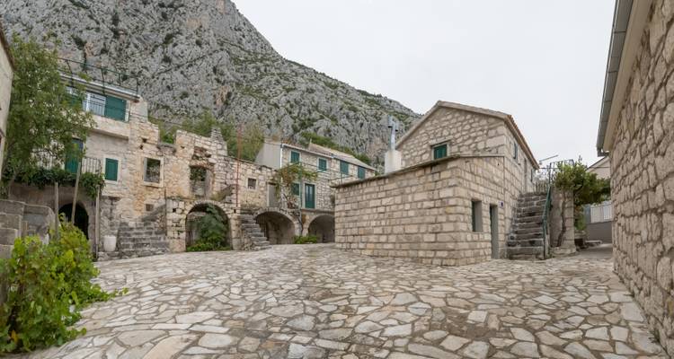 Patio de piedra silencioso de un pueblo tradicional dálmata enmarcado por montañas grises escarpadas.