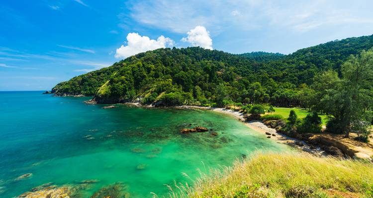 Bahía esmeralda tropical con laderas de selva exuberante y agua turquesa cristalina bajo un cielo brillante.