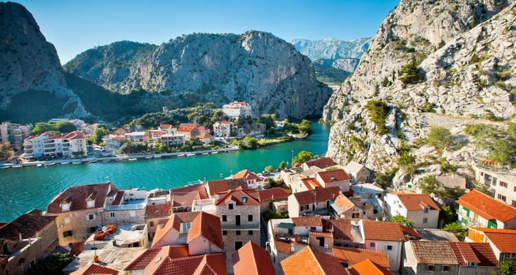 Vista aérea de un pueblo de tejados rojos enclavado entre acantilados de piedra caliza empinados y un río turquesa.