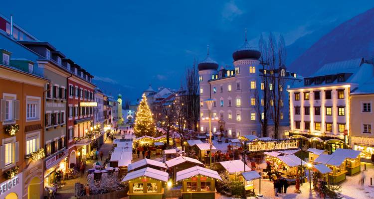 Marché de Noël alpin festif sur une place de ville enneigée avec des lumières scintillantes et des stands décorés à l'heure bleue