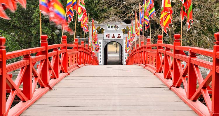 Puente de madera rojo brillante bordeado con banderas coloridas que conduce a una puerta tradicional de un templo junto al lago.