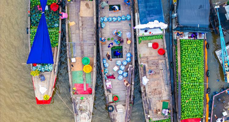 Vista aérea colorida de un bullicioso mercado flotante con botes de madera cargados de productos amarrados uno al lado del otro.