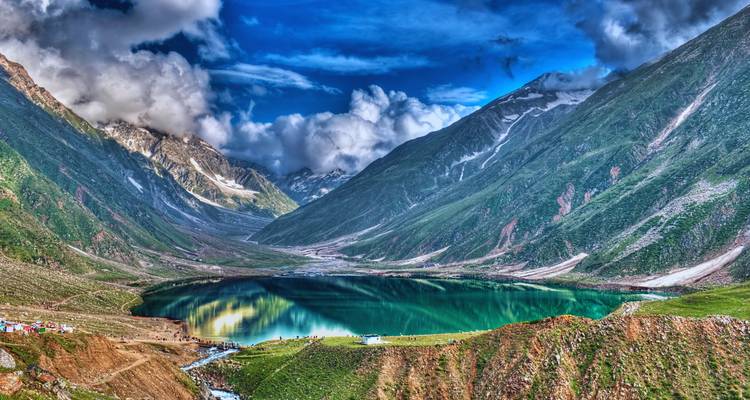 Vivid turquoise Lake Saif ul Malook encircled by rugged snow-streaked peaks under dramatic clouds.