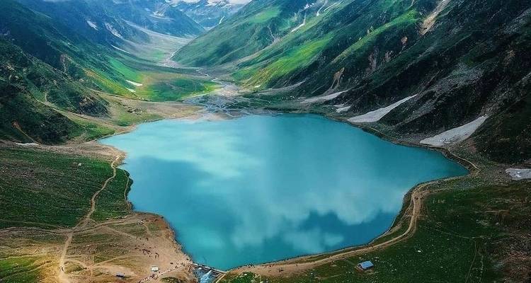 Aerial view of calm blue alpine lake surrounded by rolling green mountain slopes.