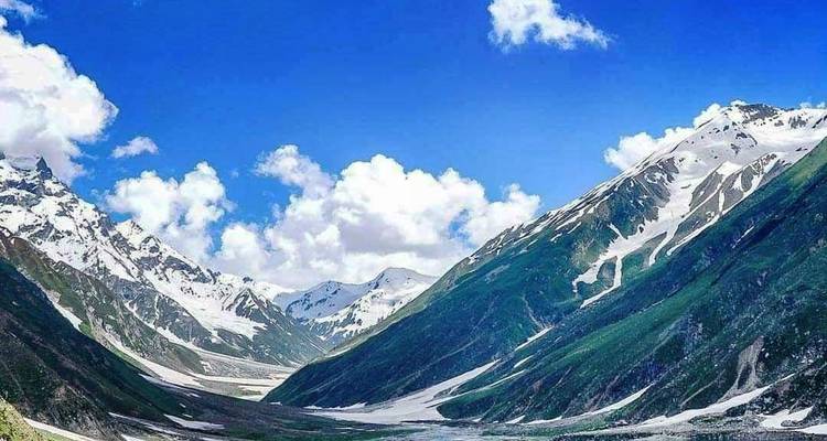 Snow-covered upper Kaghan Valley framed by bright blue sky and scattered clouds.